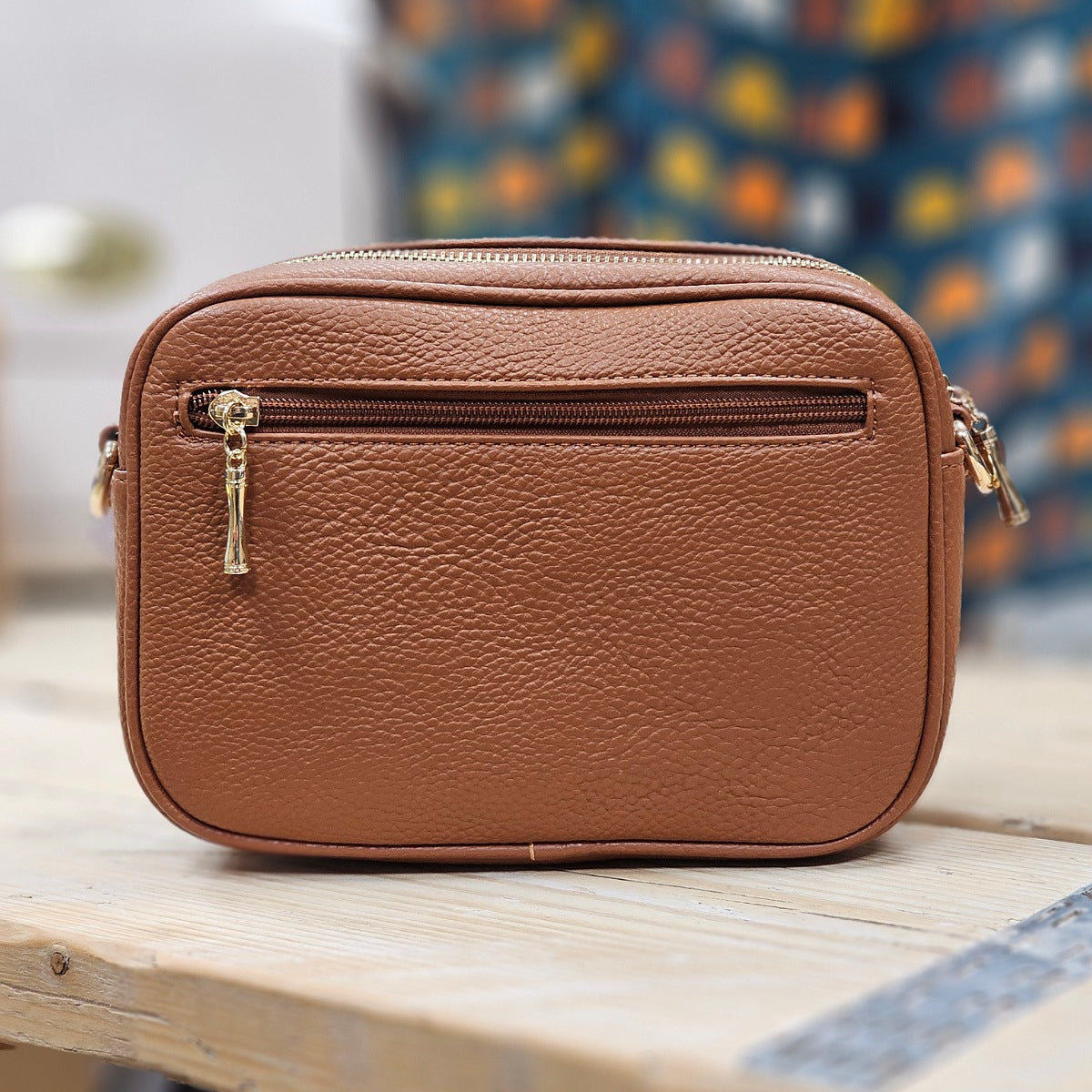 Brown crossbody bag on a wooden surface with a blurred colourful background