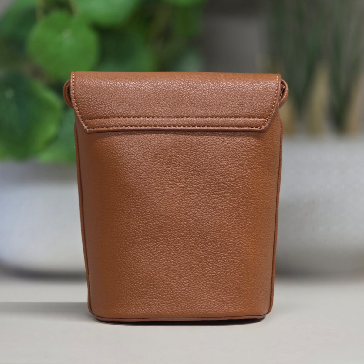 Brown leather pouch on a light surface with a blurred green plant background