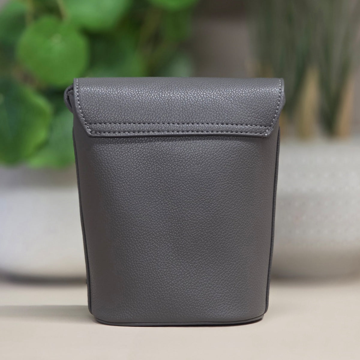 Gray leather pouch on a neutral background with blurred green plants in the background