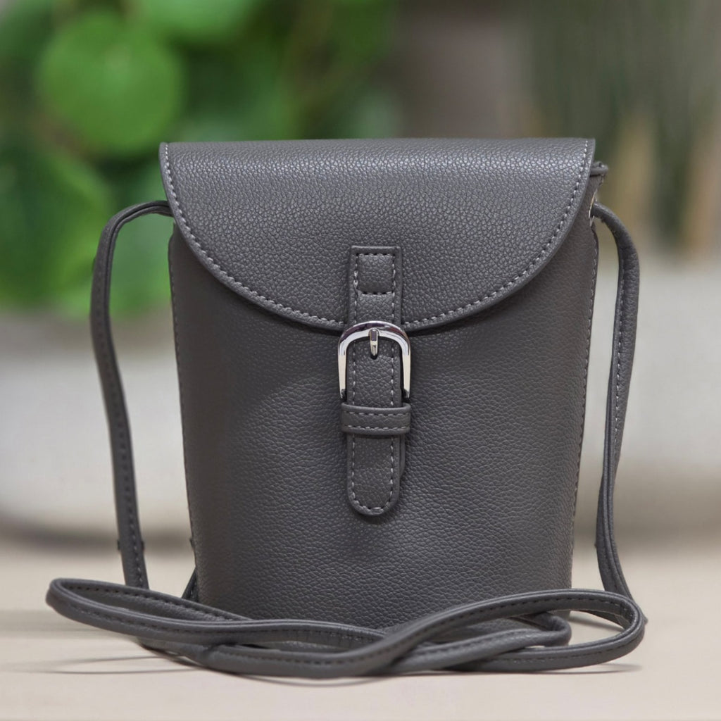 Gray leather crossbody bag with a buckle on a blurred green and brown background