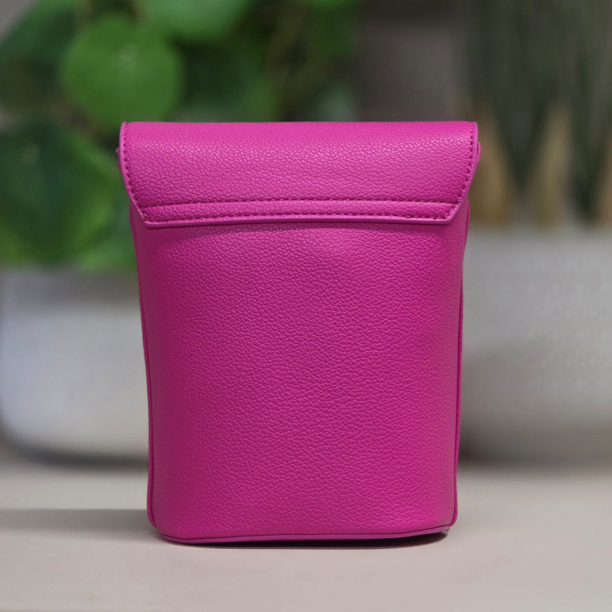 Pink leather crossbody bag with a strap on a blurred background