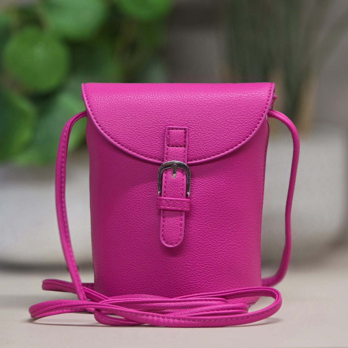 Pink leather crossbody bag with a strap on a blurred background