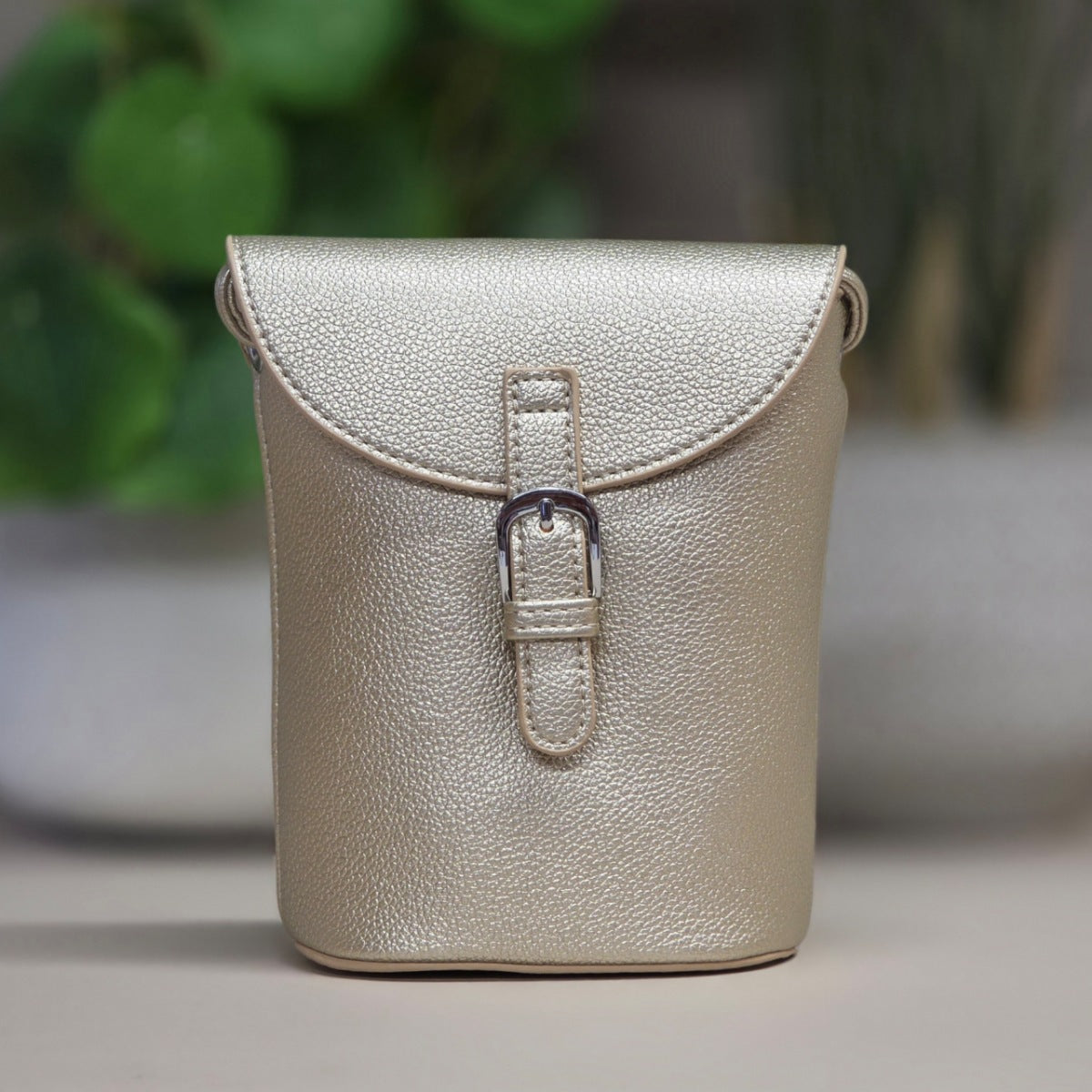 Small gold leather bag with a buckle on a neutral background