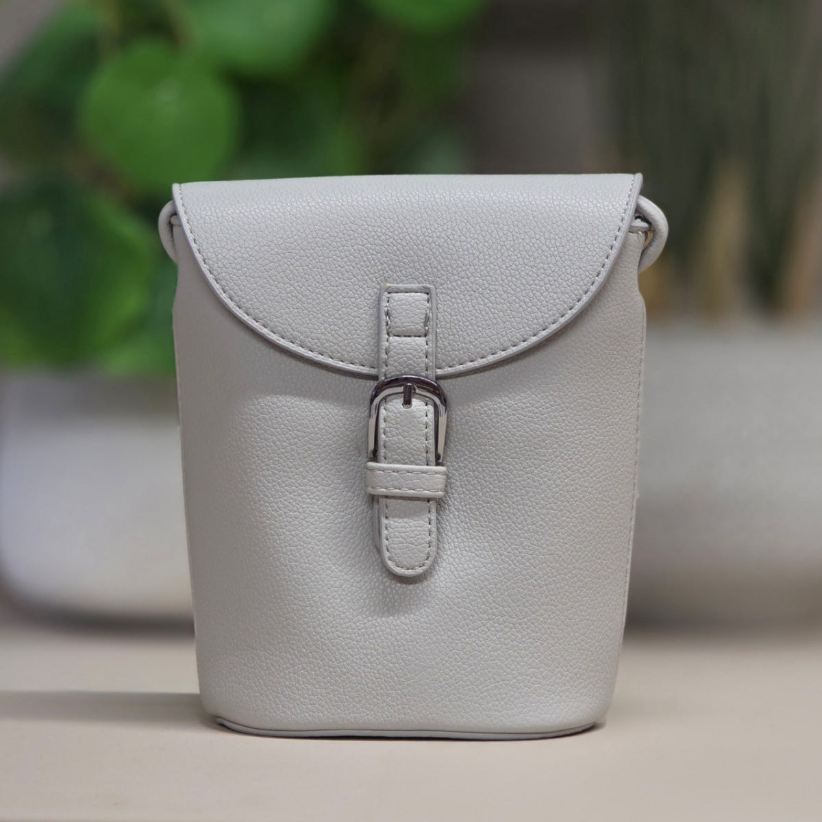 Light gray leather bag with a buckle on a blurred background