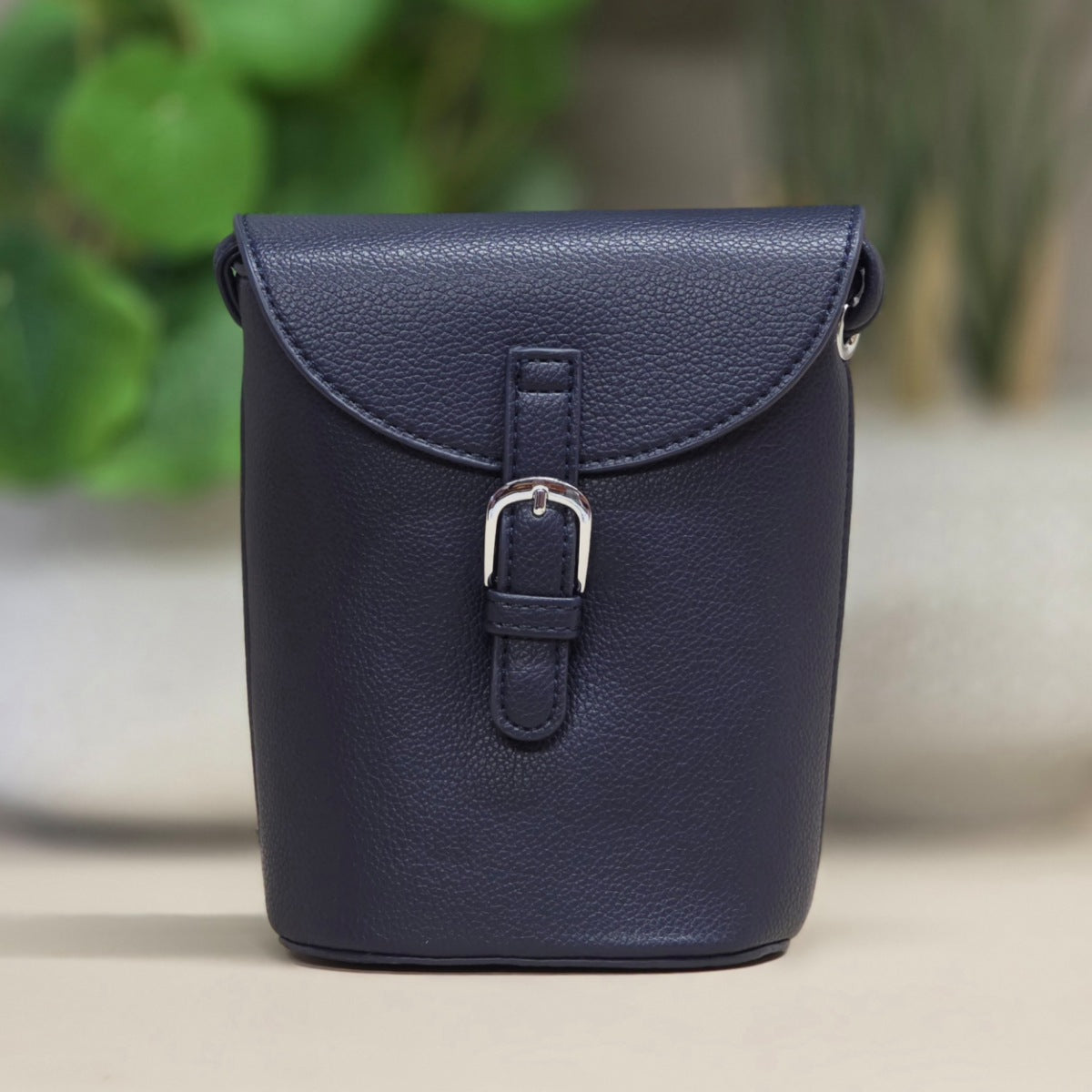 Navy blue leather bag with a buckle on a neutral background