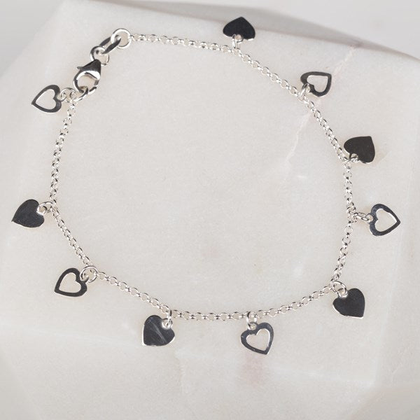 A silver chain bracelet with multiple dangling heart charms, including solid silver hearts and open heart outlines, displayed on a soft white background.