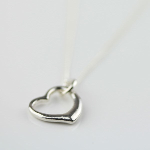 A silver heart-shaped pendant necklace on a delicate white cord, photographed against a clean white background.