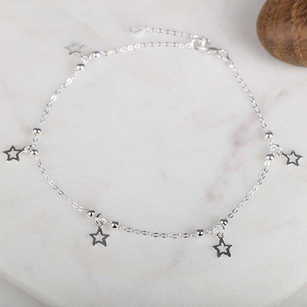 A delicate silver chain anklet featuring five small star charms, displayed on a light marble surface.