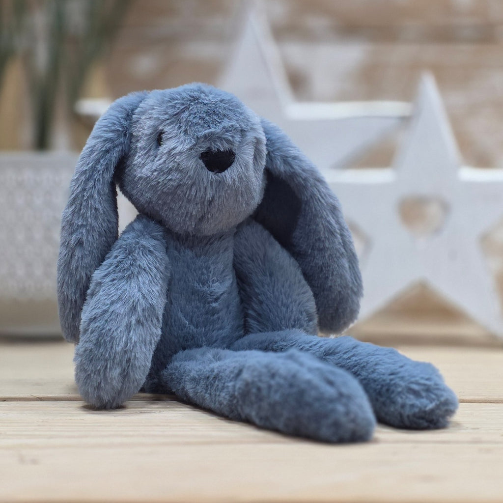 A blue soft fuzzy plush bunny toy, with black eyes and nose, on a wooden surface with a blurred star-shaped object in the background
