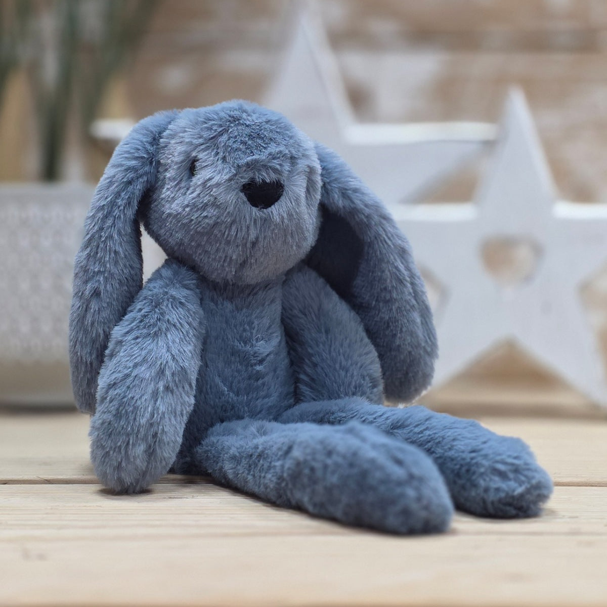 A blue soft fuzzy plush bunny toy, with black eyes and nose, on a wooden surface with a blurred star-shaped object in the background

