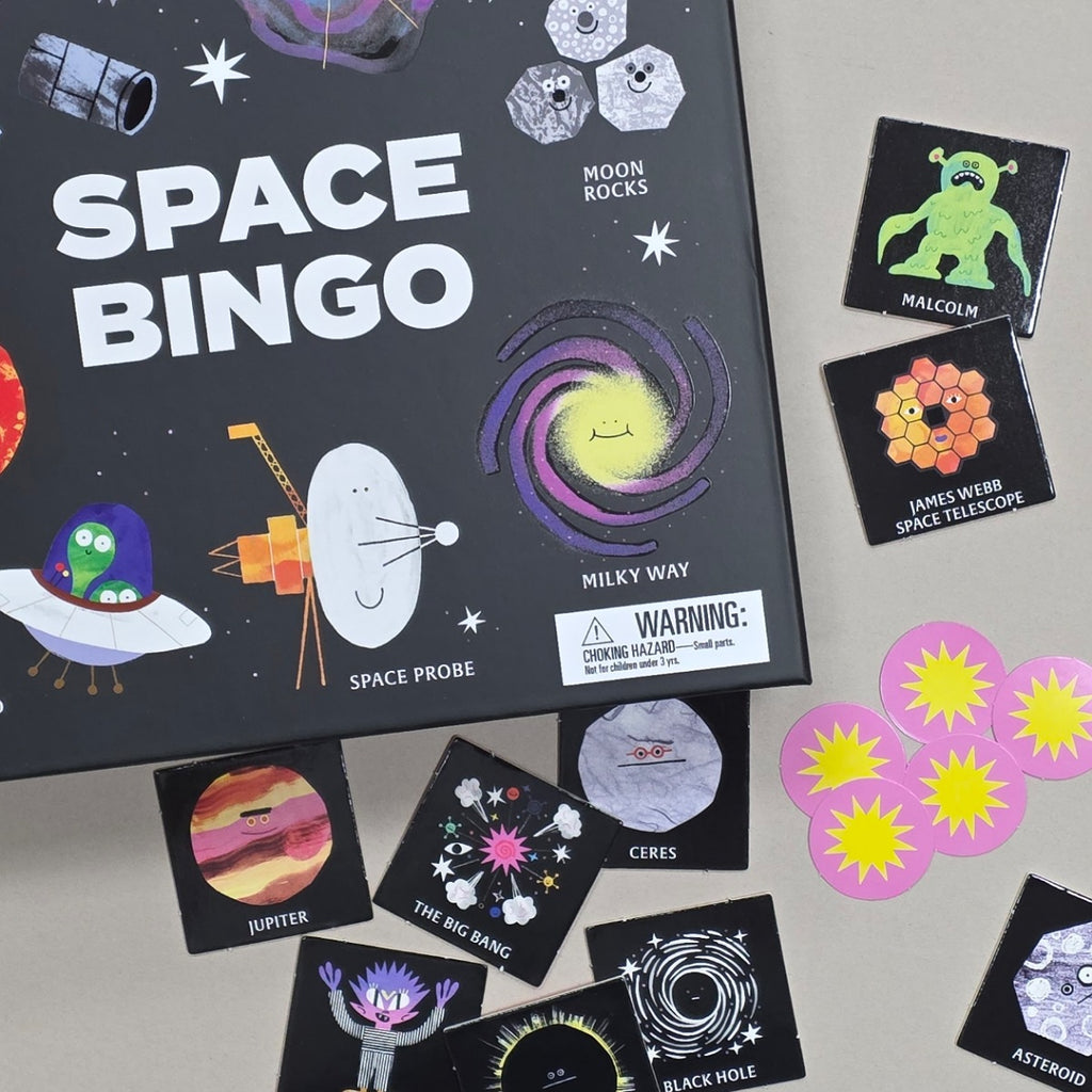 Space Bingo board game and cards arranged on a light beige surface. The black game box features colorful space illustrations and the title 'SPACE BINGO' in large white letters.