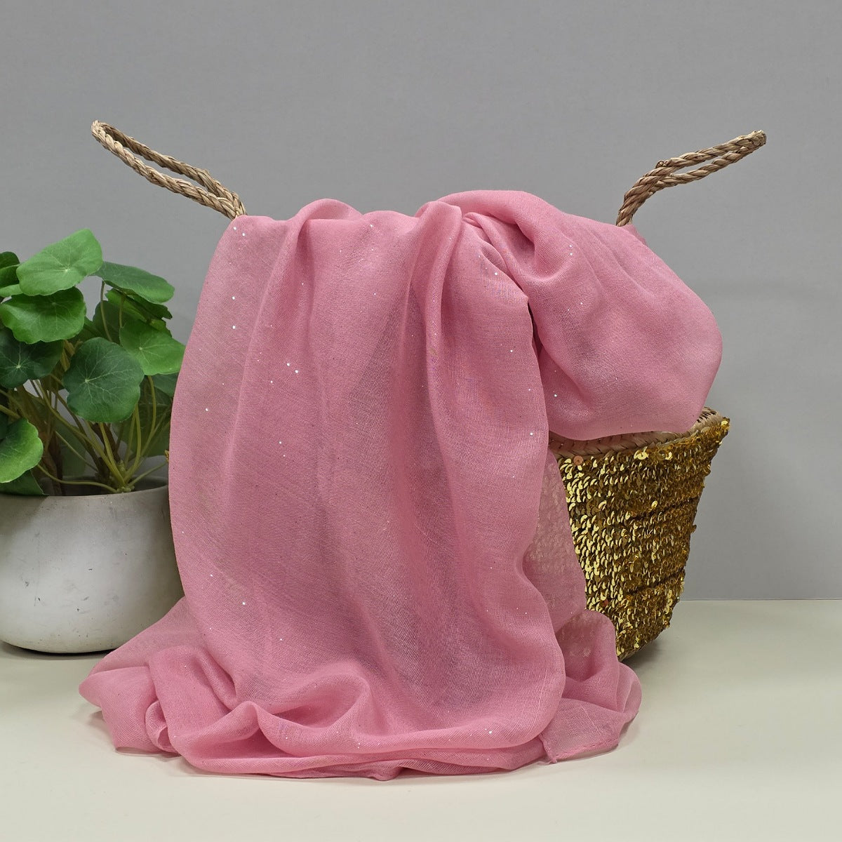 Pink lightweight fabric with glittery detail draped over a decorative basket on a neutral background