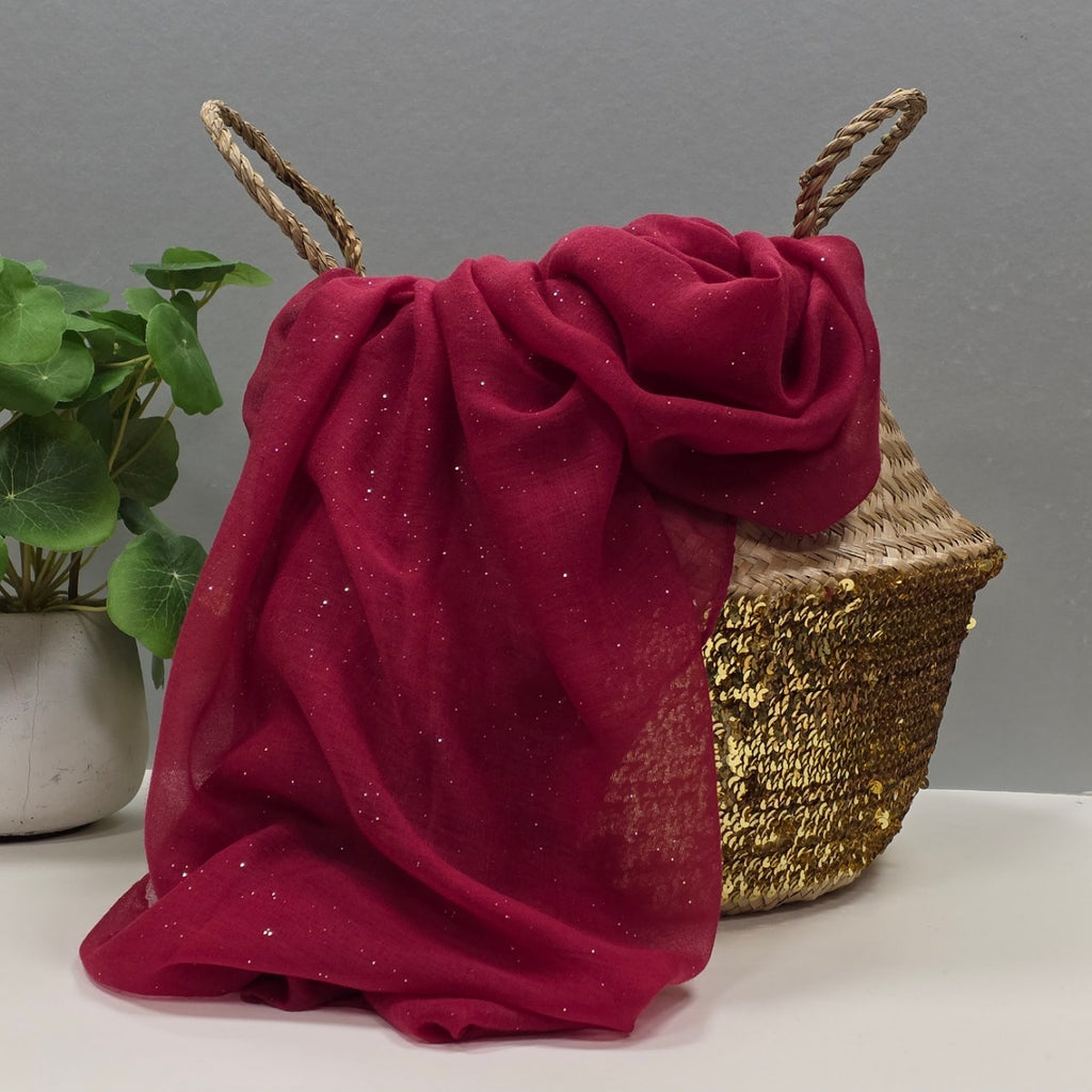 Red sheer fabric scarf with tiny sparkles on a gold sequin basket and plant on a gray background