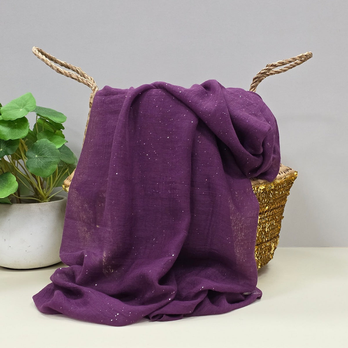 Purple lightweight scarf with tiny sparkle detail draped over a gold basket with a plant in the background