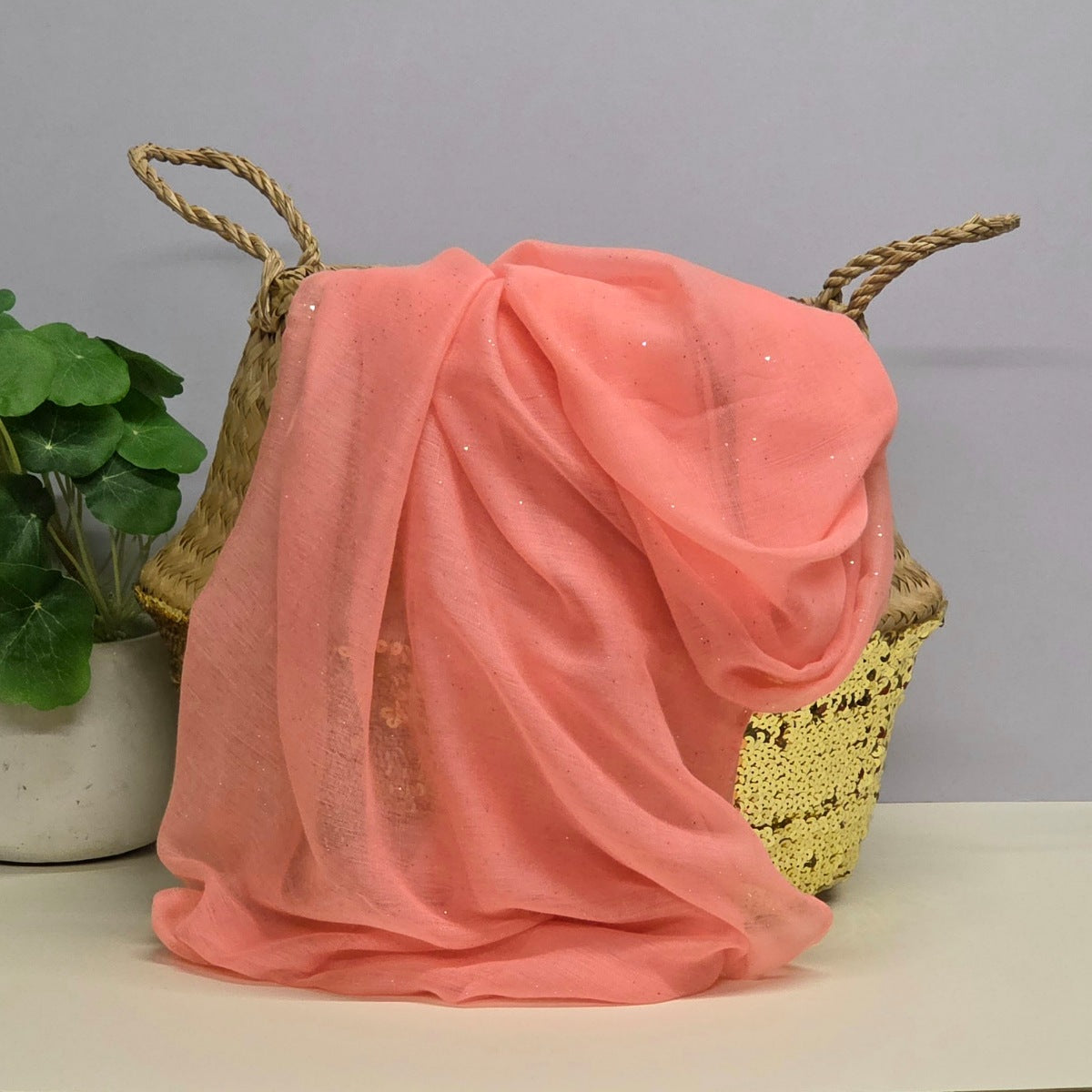 Lightweight pink scarf with gentle sparkle draped over a decorative basket with a plant in the background