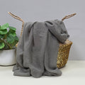 Grey lightweight scarf with gentle sparkle draped over a wicker basket with a plant in the background
