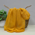Yellow lightweight scarf with gentle sparkle draped over a basket with a plant in the background