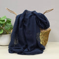 Navy blue fabric lightweight scarf with sparkle decoration draped over a basket on a light surface with a plant in the background.