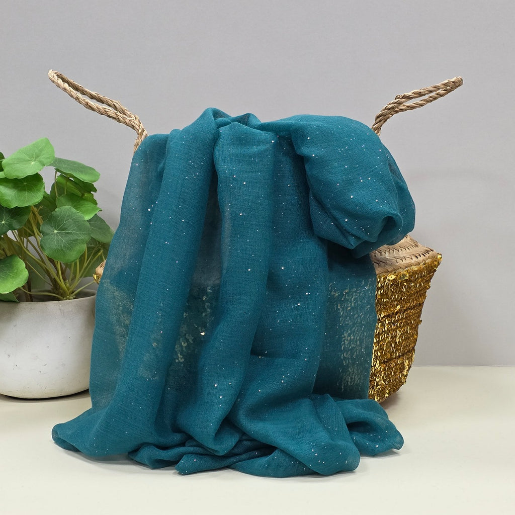 Teal fabric with a gentle sparkle draped over a wicker basket with a plant in the background