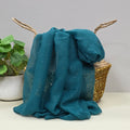 Teal fabric with a gentle sparkle draped over a wicker basket with a plant in the background