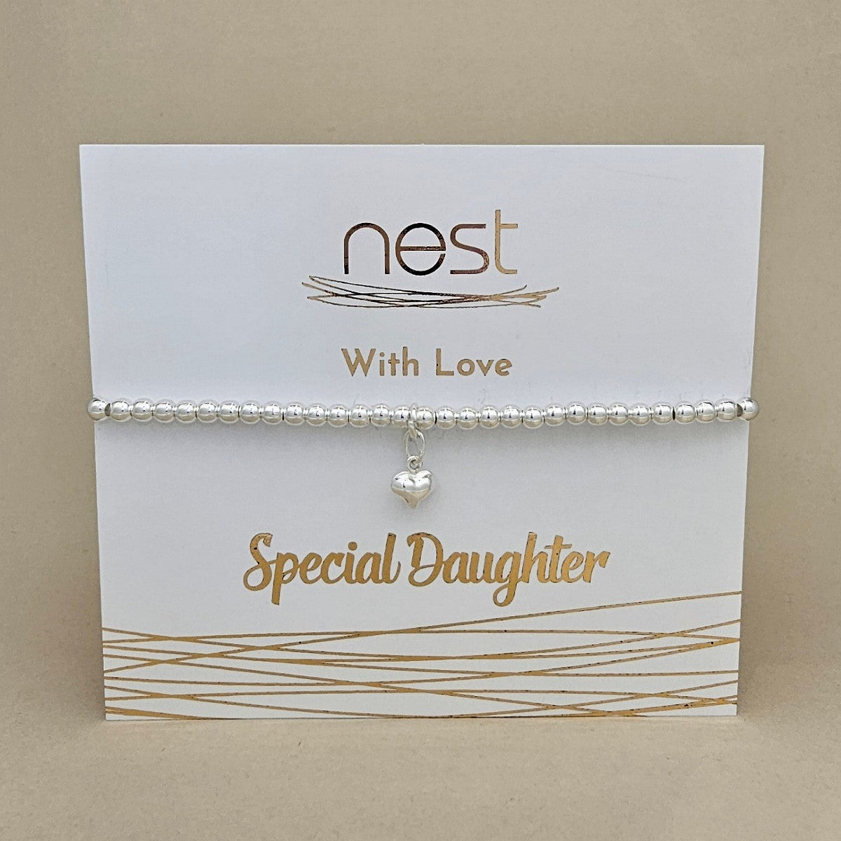 A silver beaded bracelet with a small heart charm, displayed on a white card that reads 'nest With Love Special Daughter' against a beige background.