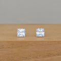 A pair of square stone earrings on a wooden base with a grey background