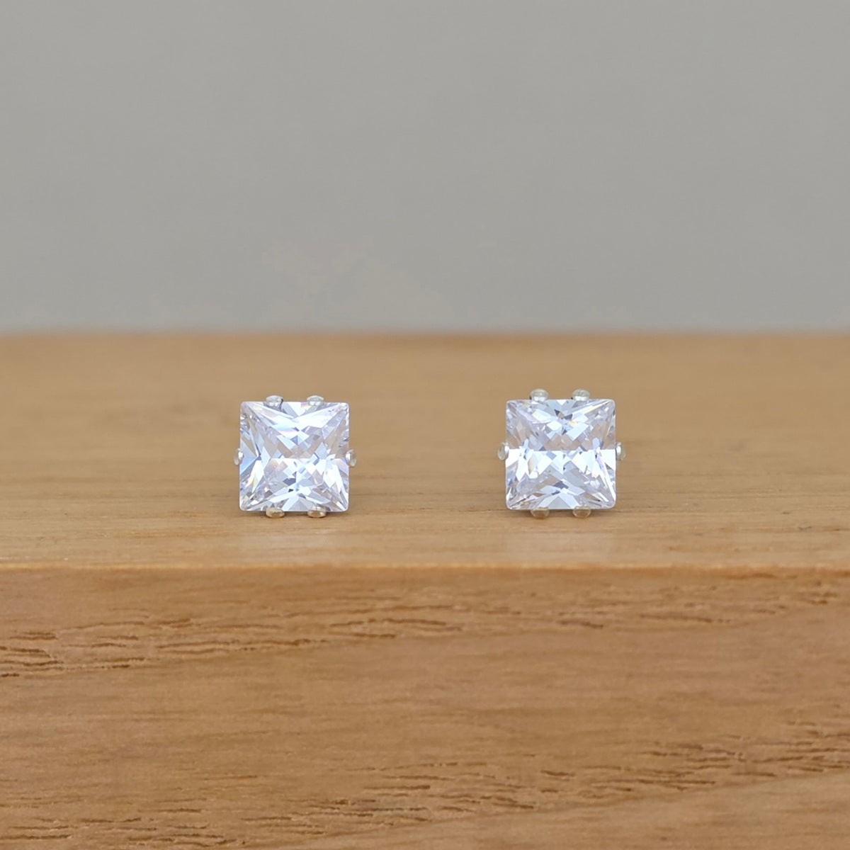 A pair of square stone earrings on a wooden base with a grey background