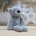 A light grey soft fuzzy plush teddy bear toy, with black eyes and nose, on a wooden surface with a blurred star-shaped object in the background
