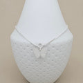 A delicate silver chain anklet with a small butterfly pendant, displayed on a textured white jewelry bust against a neutral beige background.