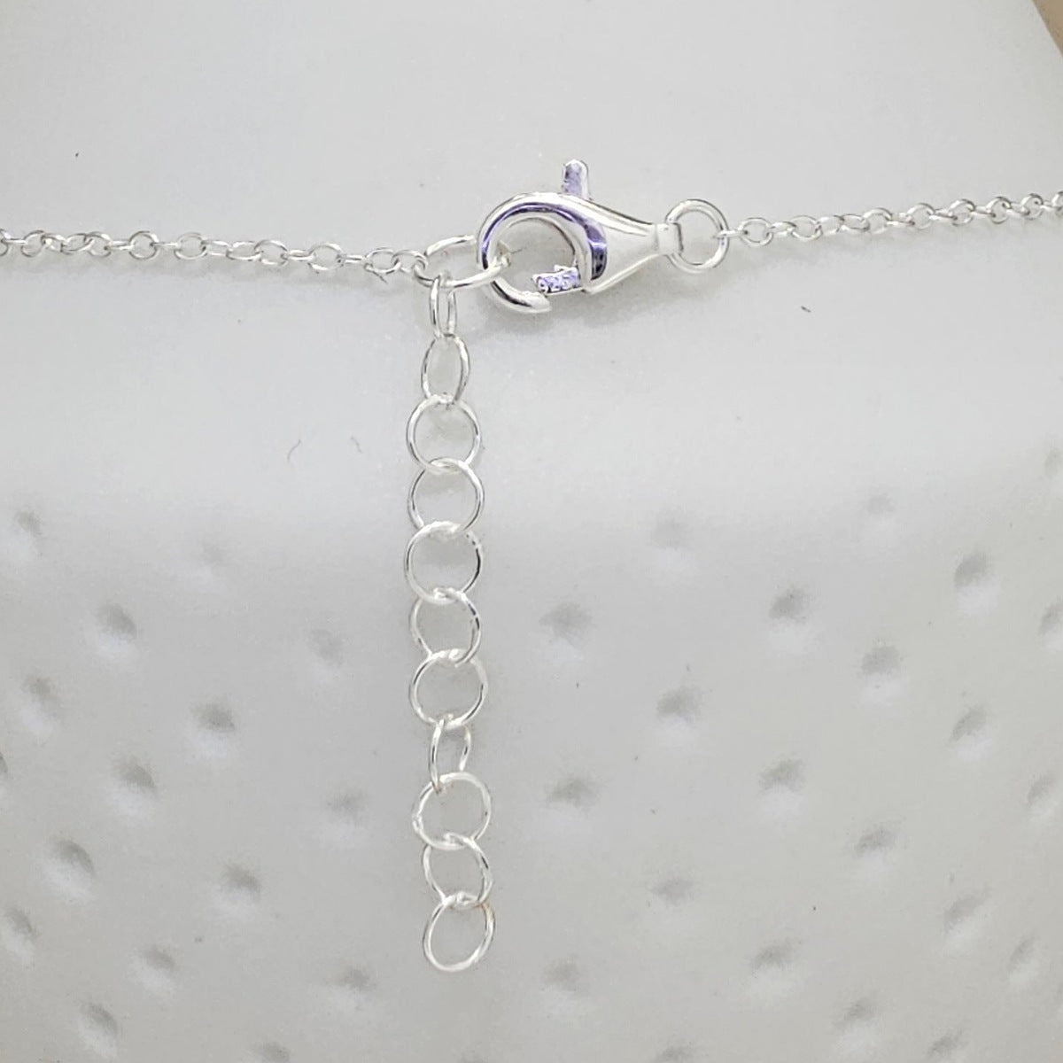 Close-up of a silver chain anklet with a lobster clasp and an adjustable link extender, displayed on a white textured surface.