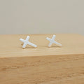 A pair of small silver cross stud earrings resting on a light wood surface against a soft beige background.