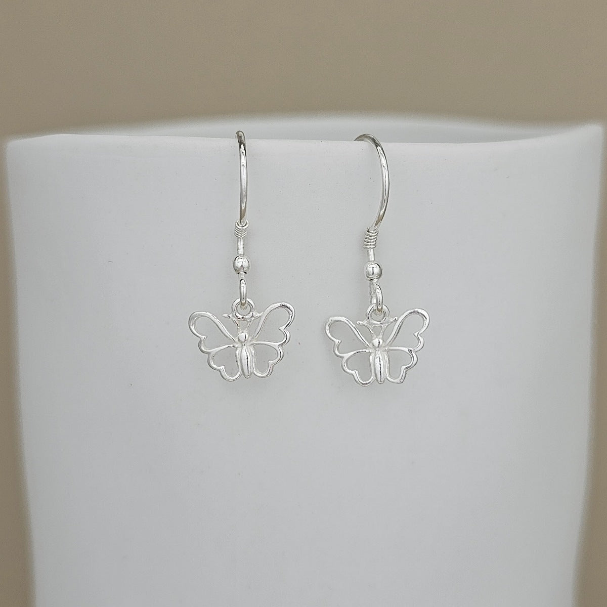 Silver butterfly earrings on a white stand with a beige background