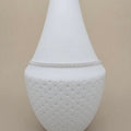 A delicate silver beaded anklet displayed on a white textured glass vase against a solid beige background.