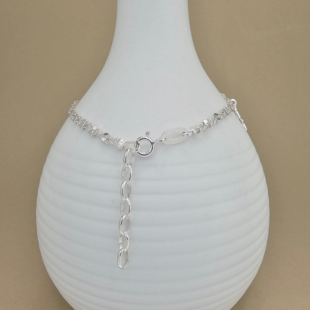 A silver-toned chain bracelet with adjustable lobster clasp, displayed on a white ribbed vase against a beige background