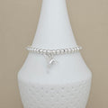 A silver beaded bracelet with a small hummingbird charm, displayed on a white ceramic jewelry bust against a neutral beige background.