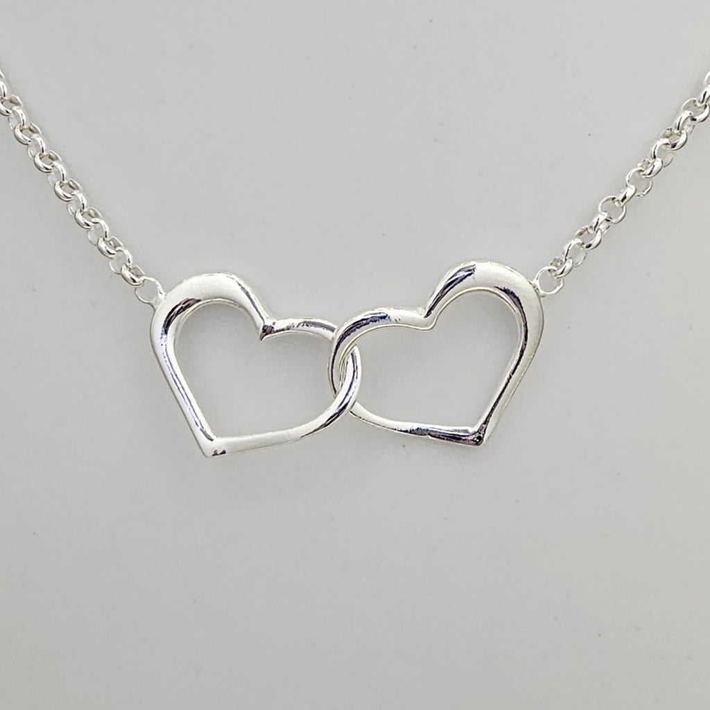 A silver necklace featuring two interlocking open heart pendants on a delicate chain, shown against a plain light gray background.