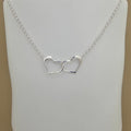 A silver chain necklace with two interlocking open heart pendants, displayed on a white mannequin bust against a beige background.