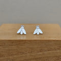 A pair of small silver moth stud earrings displayed on a wooden block against a neutral gray background.
