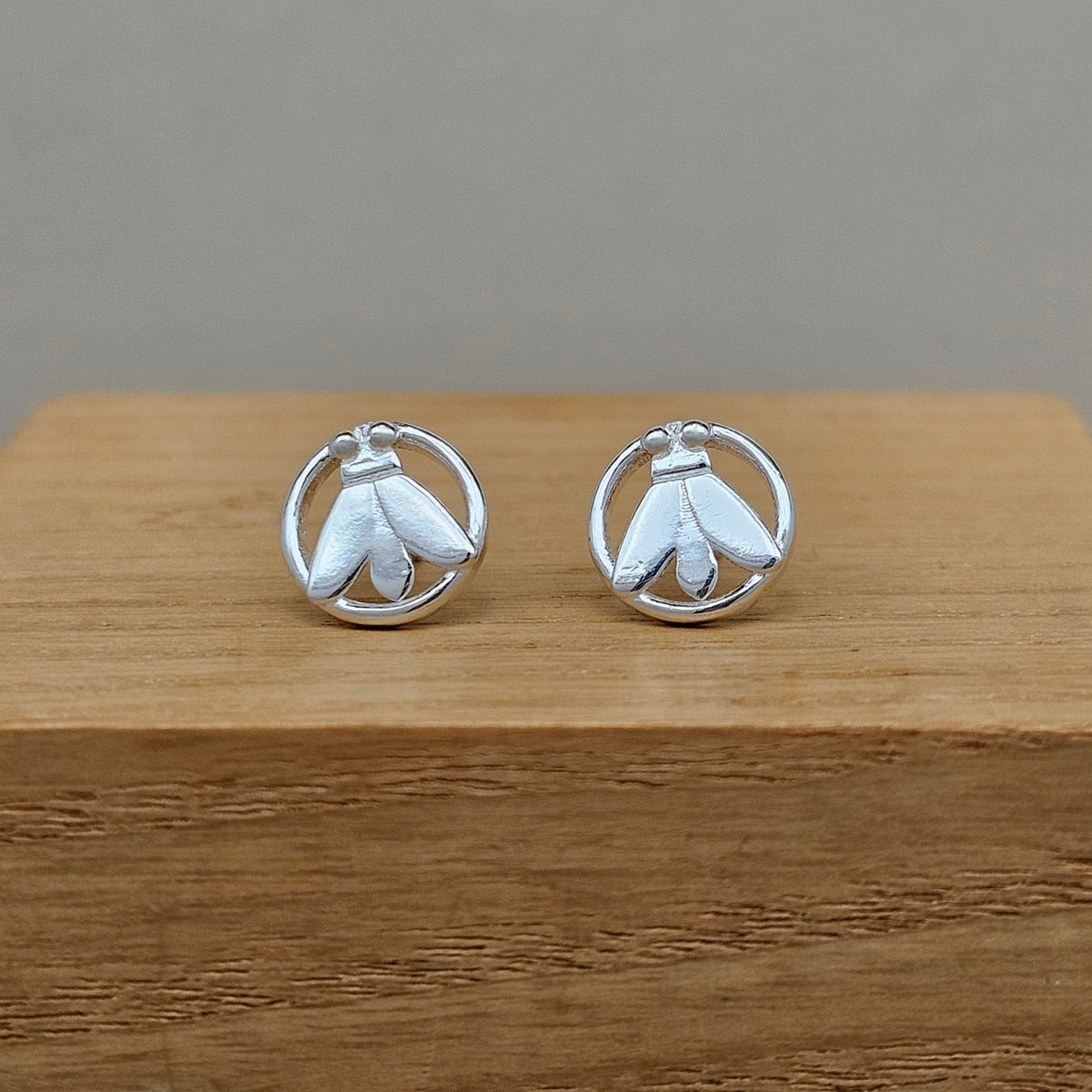 Pair of silver moth earrings on a wooden surface with a gray background