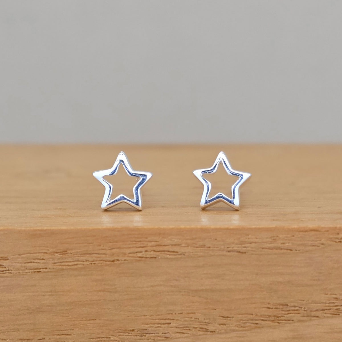 A pair of silver star-shaped stud earrings displayed on a wooden surface against a neutral gray background.