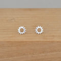 A pair of silver sunburst stud earrings displayed on a light brown wooden surface.