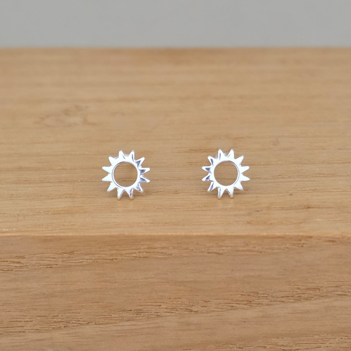 A pair of silver sunburst stud earrings displayed on a light brown wooden surface.