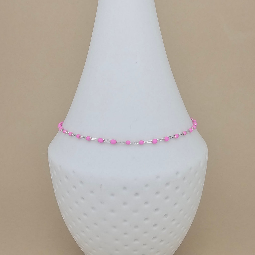 A delicate beaded anklet with pink and silver beads displayed on a white cone-shaped jewelry stand against a solid beige background.