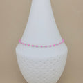 A delicate beaded anklet with pink and silver beads displayed on a white cone-shaped jewelry stand against a solid beige background.
