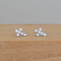 A pair of silver stud earrings with five clear round-cut stones arranged in a small cluster, resting on a light brown wooden surface against a neutral gray background.