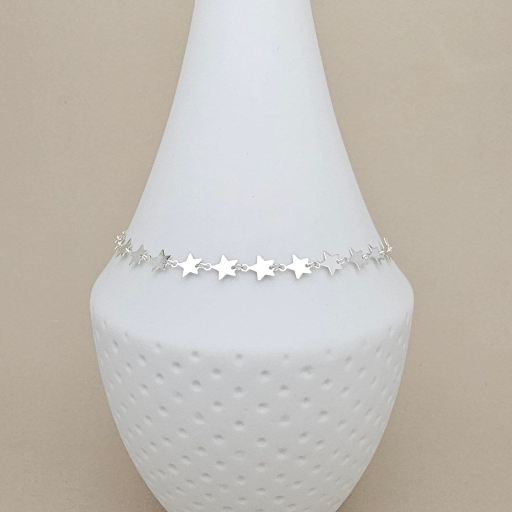 A delicate silver star chain anklet displayed on a white textured cone jewelry stand against a warm beige background.