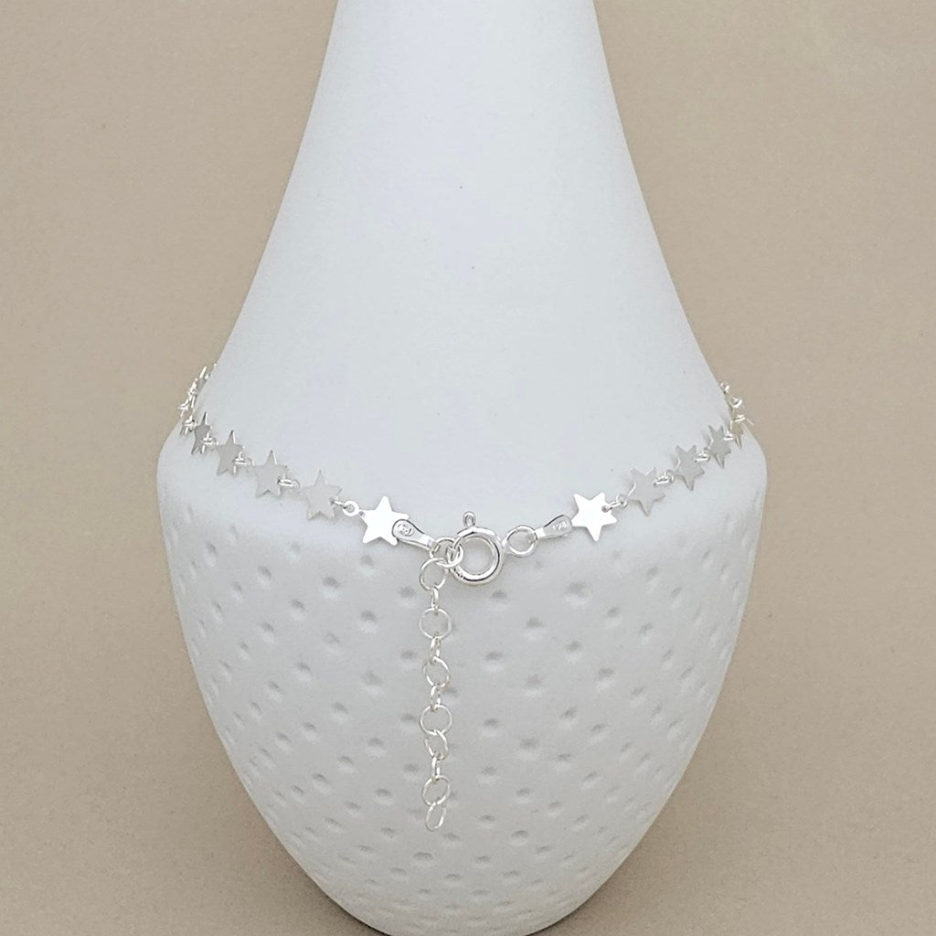 A silver star-patterned anklet displayed on a white textured cone jewelry stand against a solid beige background.