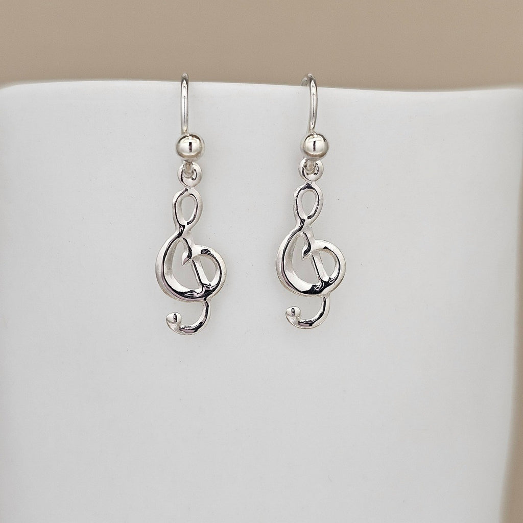 Silver treble clef earrings on a white stand with a beige background