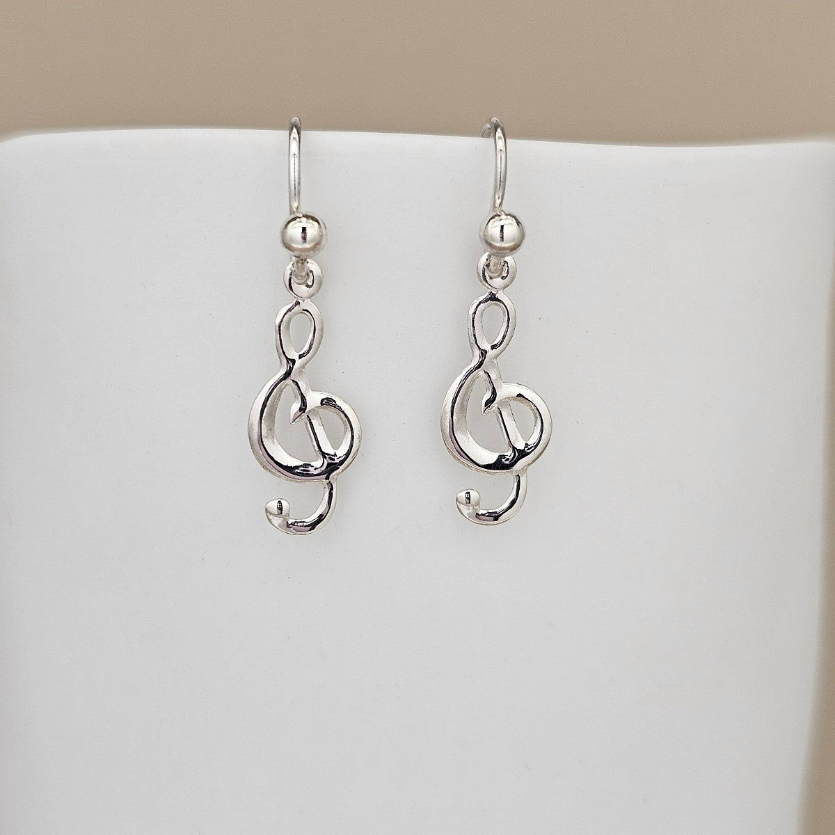 Silver treble clef earrings on a white stand with a beige background