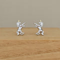 A pair of sterling silver unicorn stud earrings with gold-colored horns, displayed on a wooden block against a neutral beige background.